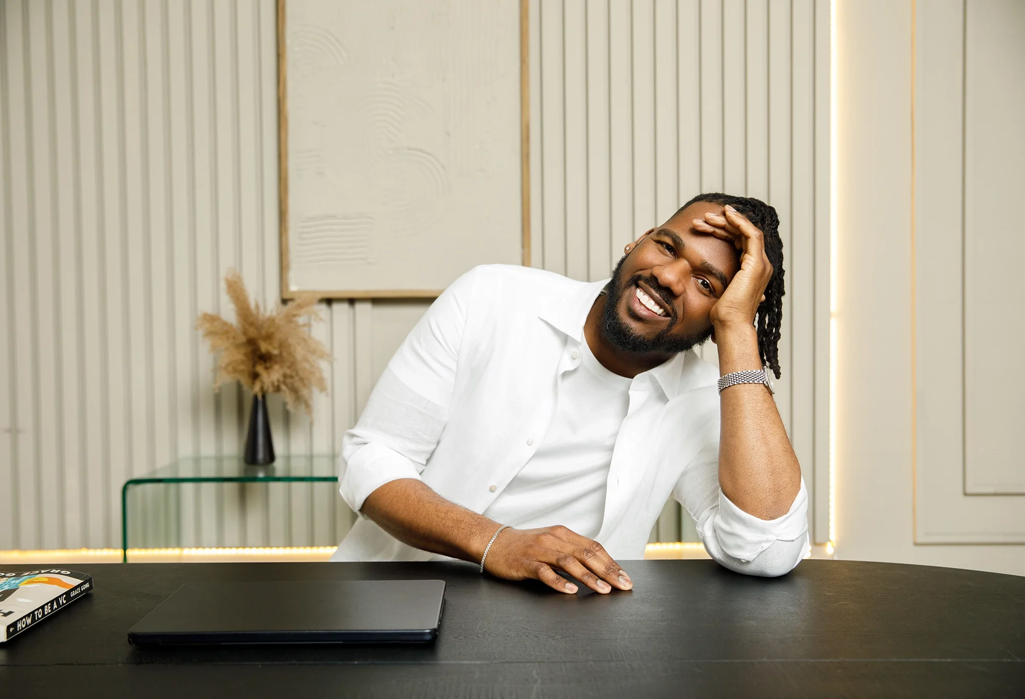 Brandon sitting at a desk, resting his head on his hand and smiling